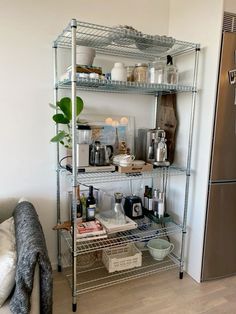 a metal shelving unit with various items on it in a living room next to a refrigerator