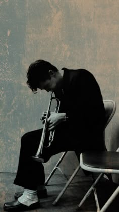 a man sitting on top of a chair holding a trumpet in his right hand and looking down at the ground