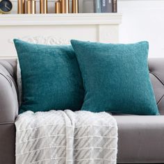 two teal pillows sitting on top of a gray couch next to a book shelf