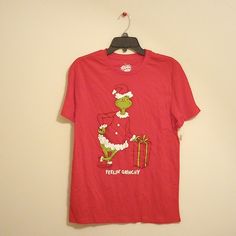 a red t - shirt with an image of the grinch holding a christmas present