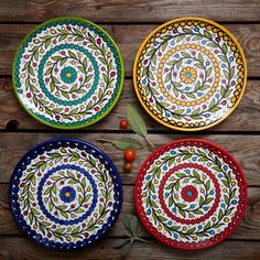 three colorful plates sitting on top of a wooden table covered in leaves and berries next to each other