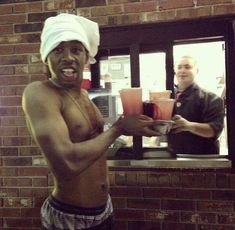 a shirtless man is holding cups in front of a brick wall and smiling at the camera