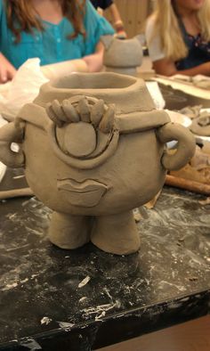 two girls are working on clay sculptures in the shape of an owl and frog, while another girl looks on