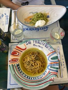 a bowl of noodles and some drinks on a table with plates, napkins and cups