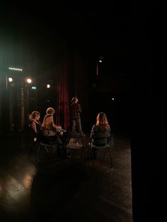 four people sitting in chairs on a stage with one person standing up and the other seated down