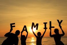 three people holding up letters that spell out the word family in front of an ocean