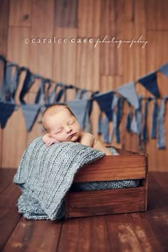 a baby wrapped in a blanket is laying on a wooden crate with blue streamers