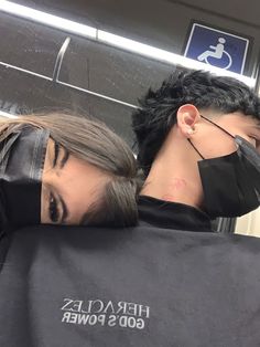 a man and woman wearing face masks while riding on a subway train with their backs wrapped around each other