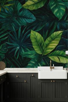 a bathroom with black cabinets and green leaves on the wall behind it is a white sink