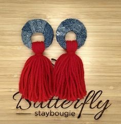 two red and blue tasselled earrings sitting on top of a wooden table with the words butterfly stay bougie