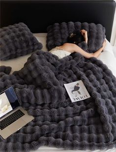 a woman laying in bed under a blanket with laptops on top of it next to her