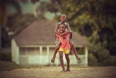 two young children are hugging each other in front of a white house with trees behind them