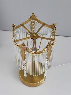 a glass and brass table lamp with chains hanging from it's sides, on a white surface