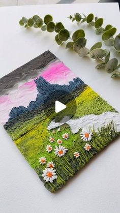 a painting with flowers on it next to a plant and some leaves in the background