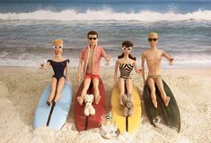 three dolls are sitting on surfboards at the beach