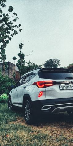 the rear end of a silver suv parked on top of a grass covered field next to trees