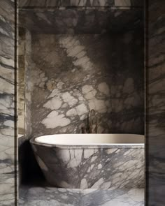 a bathtub sitting in the middle of a bathroom next to a wall with marble on it