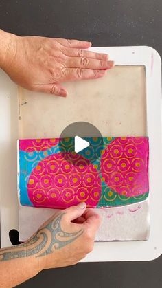 two hands are holding an art project on a white tray with pink and blue designs