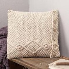 a white knitted pillow sitting on top of a wooden table