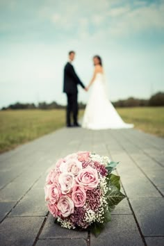 a bride and groom holding hands standing on a paved path with flowers in the foreground