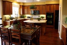 a kitchen with wooden floors and cabinets has an island table surrounded by chairs that also have potted plants on it