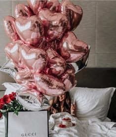 a bunch of pink heart shaped balloons on top of a bed with a woman in the background