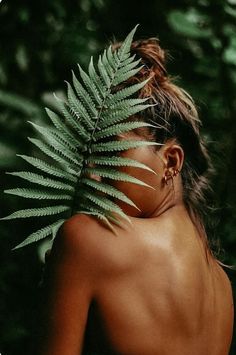 a woman with her back turned to the camera, holding a fern leaf in front of her face