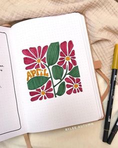 an open notebook with flowers and the words april written on it next to some markers