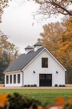 a white barn with black doors and windows in the fall season, surrounded by trees