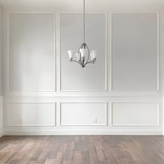 an empty room with white walls and wood flooring is pictured in this image, there are three chandeliers hanging from the ceiling