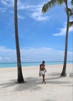 a woman walking on the beach between two palm trees