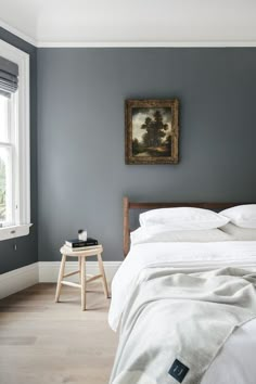 a bed with white sheets and pillows in a bedroom next to a painting on the wall