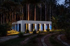 a small white building sitting in the middle of a forest at night with lights on