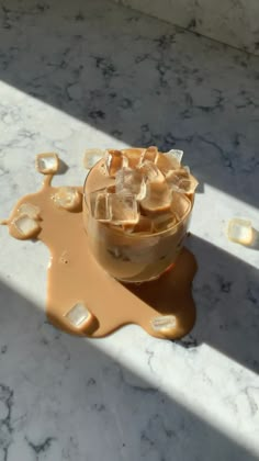 a glass filled with liquid sitting on top of a marble counter covered in ice cubes