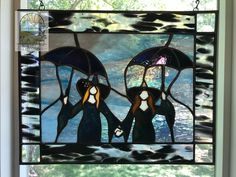 two stained glass penguins holding umbrellas in front of a window with water and trees behind them