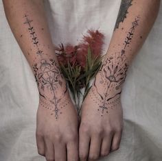 two hands with tattoos on them holding a plant and some feathers in the middle of their palms