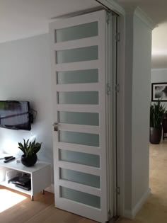 an open door leading to a living room with a television on the wall and potted plants