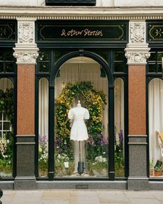 a storefront with a mannequin in front of it and flowers behind the window