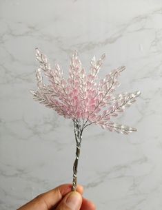 a hand holding a pink flower on top of a white marble countertop next to a wall