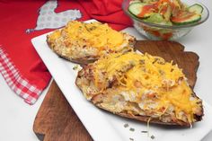 two loaded baked potatoes on a plate next to a bowl of cucumber salad