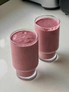 two glasses filled with pink smoothie sitting on top of a counter