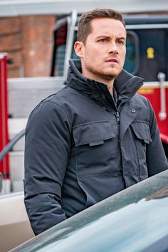 a man standing next to a parked car in front of a red firetruck