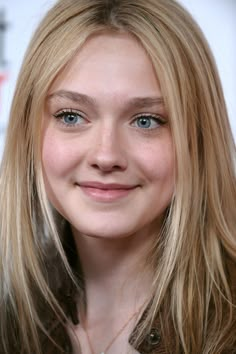 a woman with long blonde hair and blue eyes smiles at the camera while wearing a brown jacket