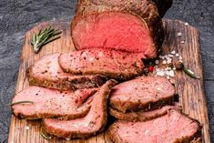 sliced roast beef on a cutting board with herbs and pepper sprinkled on top