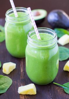 two mason jars filled with green smoothie next to avocado slices and leaves