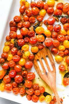 a white plate topped with lots of tomatoes and a wooden spatula next to it