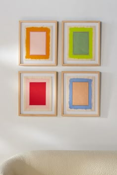 three square paintings hang on the wall above a couch in a room with white walls