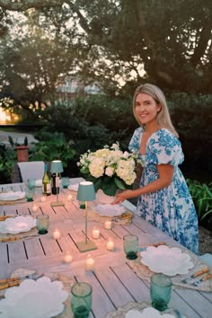 a woman is setting a table with candles and flowers