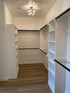 an empty walk in closet with white shelving and wood flooring on the side