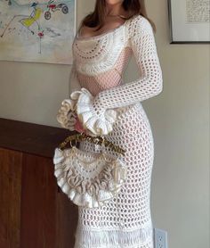 a woman in a white crochet dress holding a purse and posing for the camera